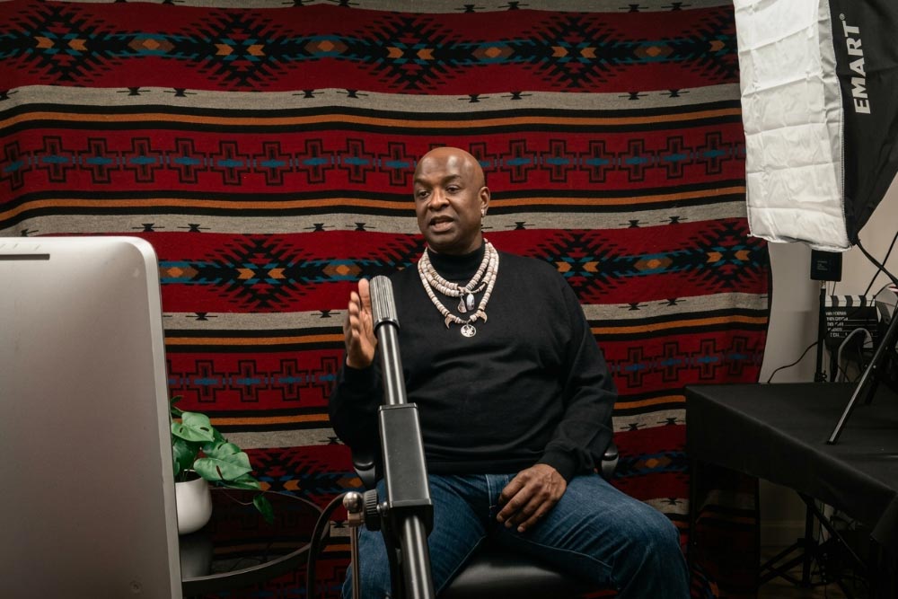 Podcast Recording Session Person speaking into a microphone during a podcast recording, seated in front of a patterned blanket backdrop.
